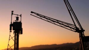 A close-up of a radio tower at sunset, with the silhouettes of Fort Collins and Boise in the background, symbolizing the upcoming changes in the radio landscape.