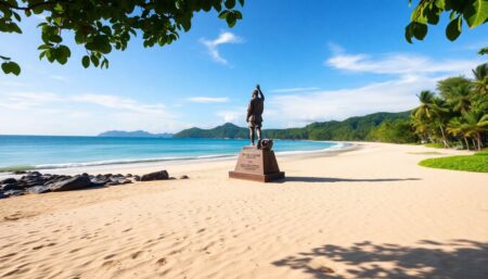 Generate an image of a serene beach in Southeast Asia with a memorial statue commemorating the 2004 Indian Ocean tsunami, surrounded by lush greenery and a clear blue sky.